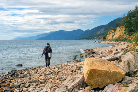 The fisherman walks along the shore of a large lake with fishing tackleの写真素材