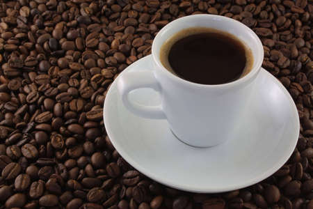 White cup of coffee on a saucer and coffee grains