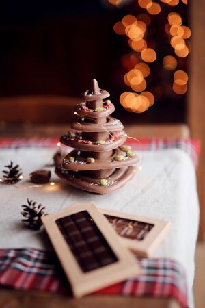 Christmas tree made of natural chocolate stands on the festive table against the background of lights, cozy home atmosphereの写真素材