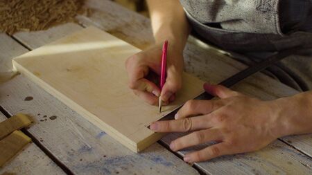 20s bearded man carpenter drawing on wooden board. sunny day in workshop. handcrafting concept...