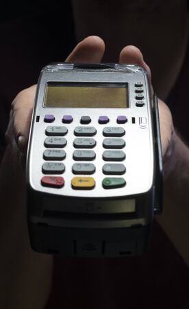 Credit card reader isolated on black background. Pos apparatus for non-cash contactless payment. A man holds an NFC terminal in his handsの写真素材