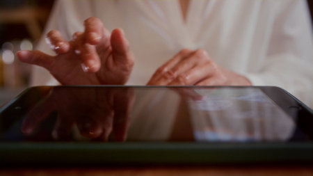 An old woman scrolls photos on a tablet in a cafe. Senior female looks at photos in a restaurant, touches the touch screen with her fingers. The concept of modern technologies.の写真素材
