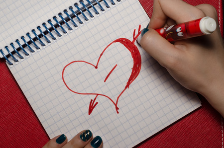 The girl drawing heart pierced by an arrow a marker in  notebooの写真素材