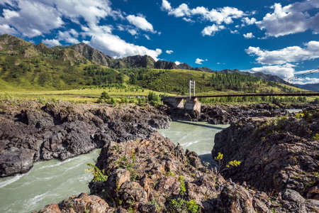 Chemalsky district, Altai Republic, southern Siberia, Russia-August 19, 2020: Oroktoysky automobile suspension bridge over the Katun river surrounded by mountains and stone pyramidsのeditorial素材
