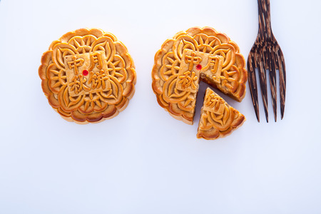 Two Mooncake with one cut up to show egg yolk for the chinese Mid-Autumn festival and wooden fork on white backgroundの写真素材