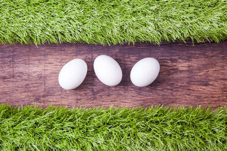 three white easter eggs laying on wooden table top and decorated with green grassの写真素材