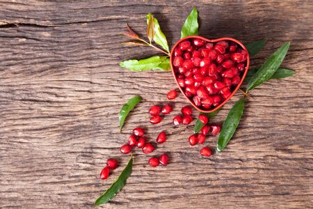 fresh pomegranate seeds in heart shaped with leaf on wooden table topの写真素材