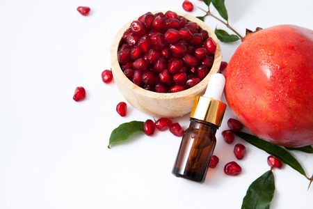 serum bottle or essential oil bottle with fresh pomegranate isolated on white backgroundの写真素材