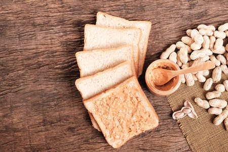 chunky peanut butter on whole wheat bread and peanut butter in jar on wooden table top