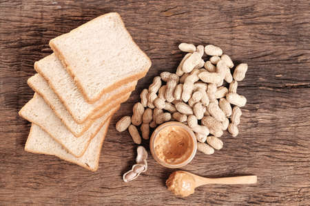 peanut butter in jar and whole wheat bread on wooden table topの写真素材