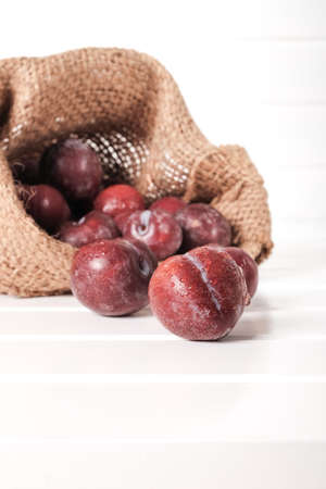 Fresh red plums in sack isolated on white wooden table topの写真素材