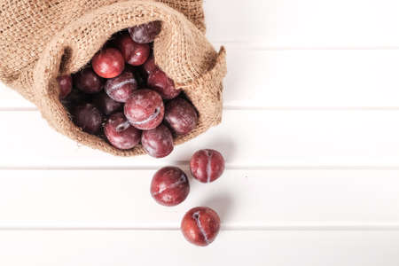 Fresh red plums in sack isolated on white wooden table topの写真素材