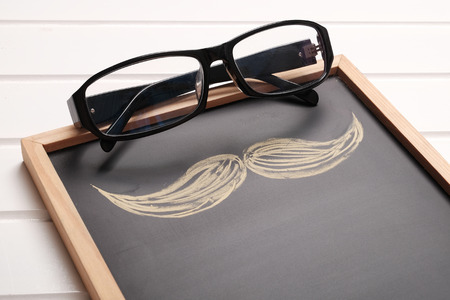 Glasses and mustache hand drawn on chalkboard. On white wooden table topの写真素材