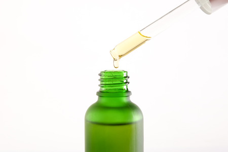 Essential oil drop from dropper to green bottle on white background.の写真素材