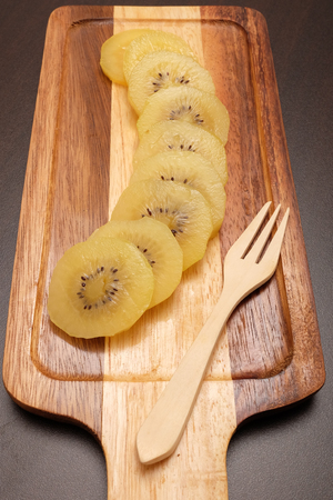 Healthy, eating and diet concept; Idea with slice of ripe yellow kiwi(or gold kiwi) in wooden plate on dark table top.の写真素材