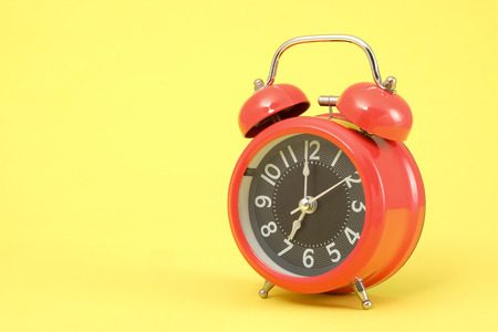 Red vintage alarm clock with space for text on yellow background.