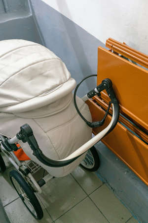 The baby stroller is stored in a public entrance, fastened with a lock to the radiator