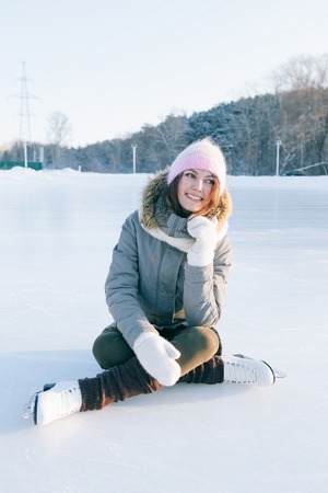 Ice skating woman sitting on the ice smiling.