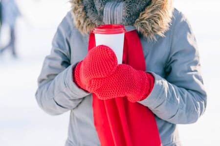 Woman holding winter cup close up on light background. Woman hands in teal gloves holding a cozy mug...