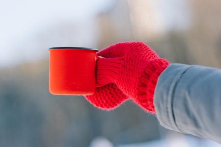Woman holding winter cup close up on light background. Woman hands in teal gloves holding a cozy mug with hot cocoa, tea or coffee and a candy cane. Winter and Christmas time concept.の写真素材