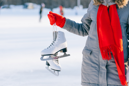 Young woman showing ice skates for winter  ice skating sport activity in white hat smiling isolated on a white backgroundの写真素材