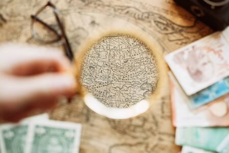 Vintage compass, magnifying glass, pocket watch, spyglass lie on an old ancient map with a lit candleの写真素材