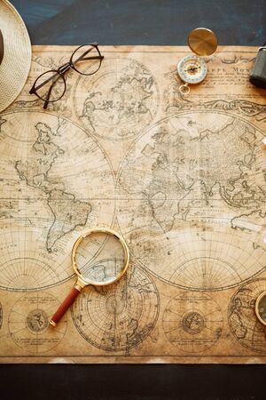 Vintage compass, magnifying glass, pocket watch, spyglass lie on an old ancient map with a lit...