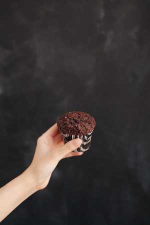 Woman holding a chocolate muffin on black background.の写真素材
