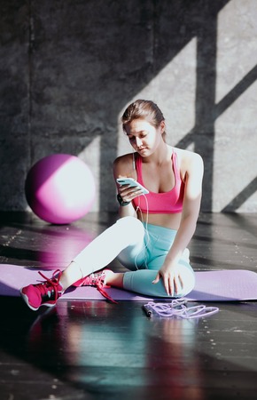 Young fit woman in pink clothes using smartphone at gym
