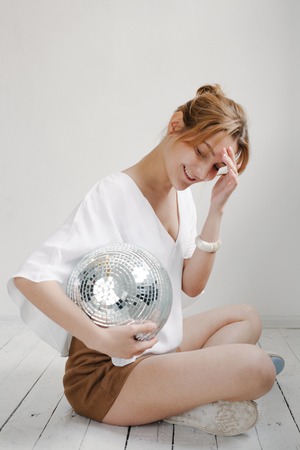 Young hipster woman holding disco ball and posing cheerfully on white background.