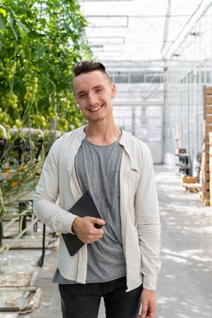 man holding clipboard and examining harvest of tomatoes in greenhouseの写真素材