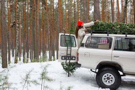 Beautiful woman in warm cozy clothes sitting on red vintage car covered with snow. Cold happy winter day. Holidays, christmas, winter, love, beauty conceptの写真素材