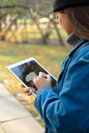 Beautiful young female student is studying using a tablet in a park. Recreation and study concept