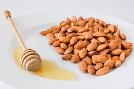 Nuts and honey photoset. A handful of almonds on a plate with honey and honey spoon isolated on a white backgroundの写真素材