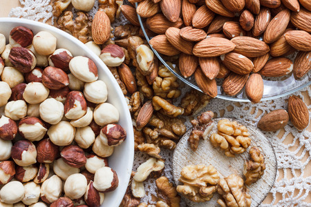 Nuts and honey photoset. Walnut, almond and hazelnut on a plates on a table with lace napkinの写真素材