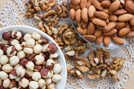 Nuts and honey photoset. Walnut, almond and hazelnut on a plates on a table with lace napkinの写真素材