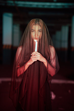 Young woman in a black robe with a burning candle in her hands