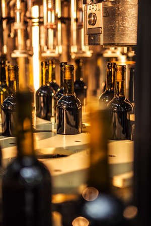 Unlabeled glass bottles in bottling machine at modern winery.の写真素材