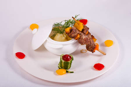 Pork skewer served with mashed potato and decorated with cucumber on white plateの写真素材