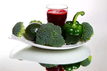 Beetroot smoothie in a large glass, near fresh broccoli, green pepper, avocado on white backgroundの写真素材