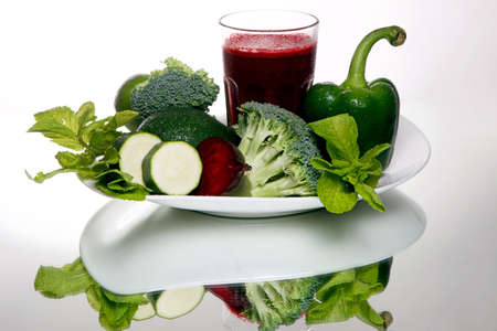 Beetroot smoothie in a large glass, near fresh broccoli, green pepper, avocado, mint and zucchini on white backgroundの写真素材