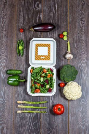 Background of wooden planks black color with fresh autumn vegetables and open white box in the middle.の写真素材