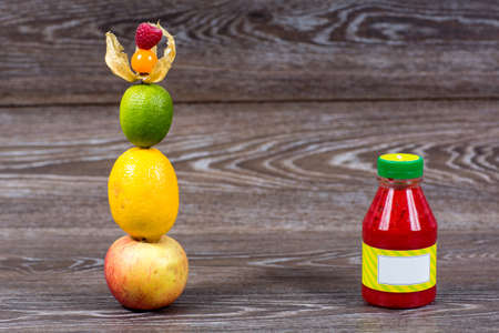 Bottle smoothie with fresh apple, lemon, lime, physalis, raspberries on wooden tableの写真素材