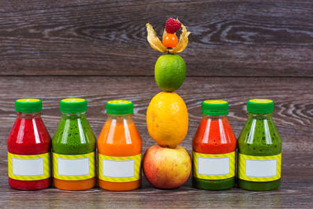 Bottles smoothie with fresh apple, lemon, lime, physalis, raspberries on wooden tableの写真素材