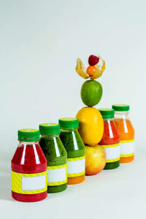 Bottles smoothie with fresh apple, lemon, lime, physalis, raspberries on white backgroundの写真素材