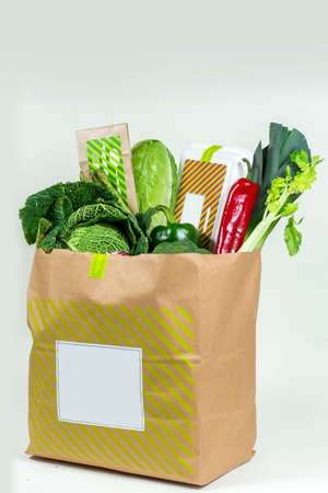 Various fresh greens, vegetables and white box in paper bag on white backgroundの写真素材
