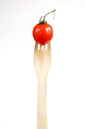 Little red fresh tomato on a wooden fork isolated over white backgroundの写真素材