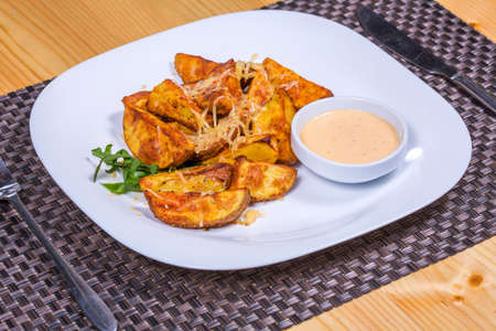 Baked spicy potatoes with cheese served since sauce and herbs on white plate, close-upの写真素材