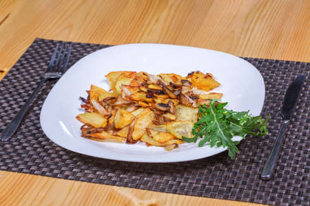 Roasted potato and mushrooms with greens in white plate on the tableの写真素材