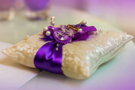 Two golden wedding rings on purple and white small satin pillow with stones and lace.の写真素材